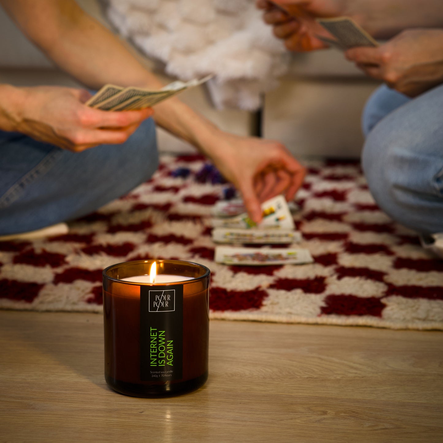 Two people counting money with a lit candle on a wooden floor.
