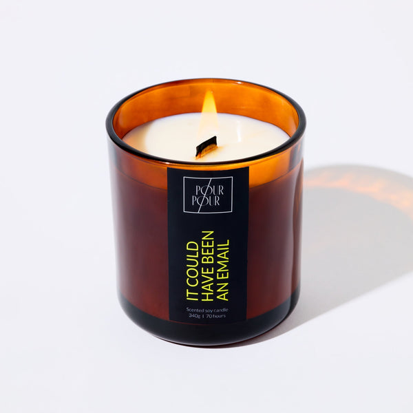 Candle in an amber glass jar with a visible brand label on a white background