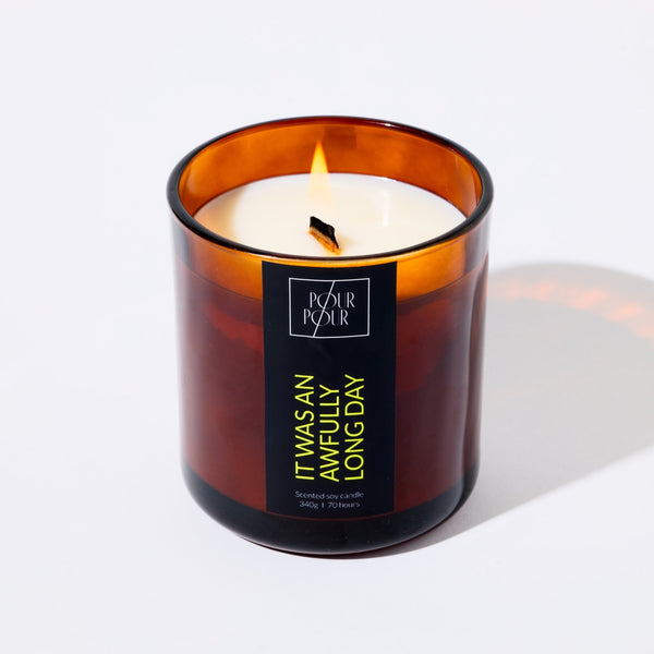 Candle in an amber glass jar with a visible brand label on a white background