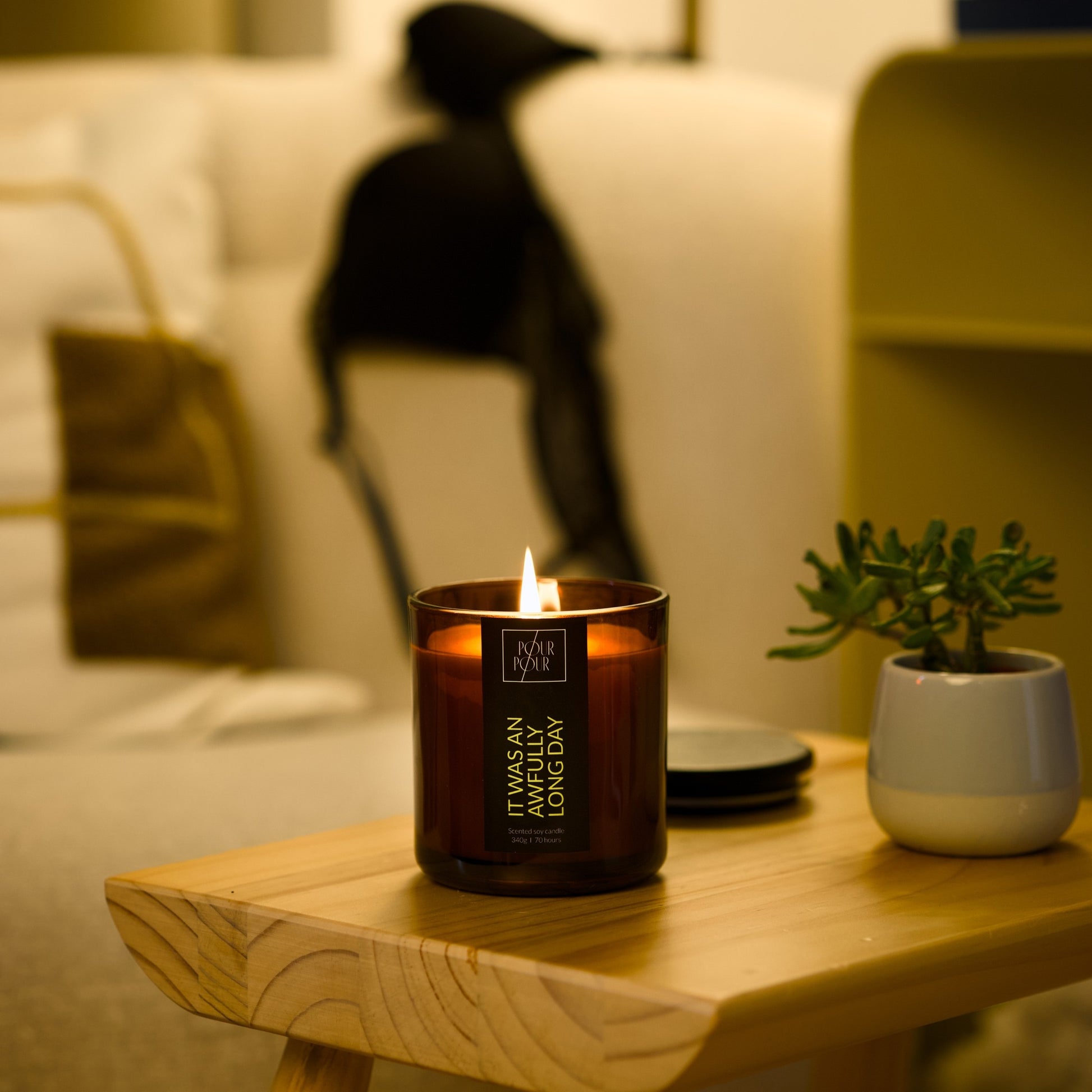 Candle on a wooden table with a blurred background of a person sitting on a couch.