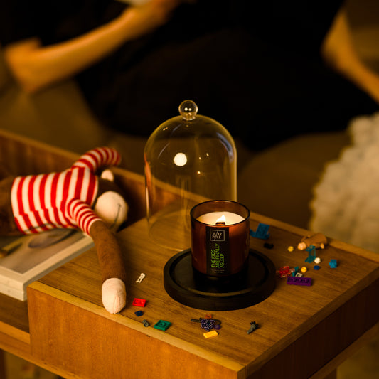 Candle in a glass dome on a wooden surface with toys and books in the background